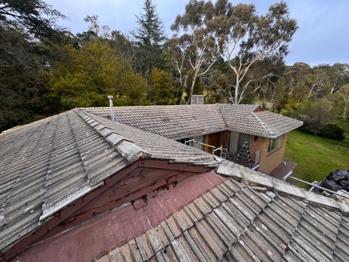 Weathered concrete tile roof with a peeling red gable, before the re-roof